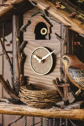 Imagem de um relógio cuco clássico, com entalhes em madeira e um pequeno pássaro do lado de fora. O design remete à tradicional história do relógio cuco, popularizado na Floresta Negra, Alemanha, representada pelos galhos secos do lado de fora.