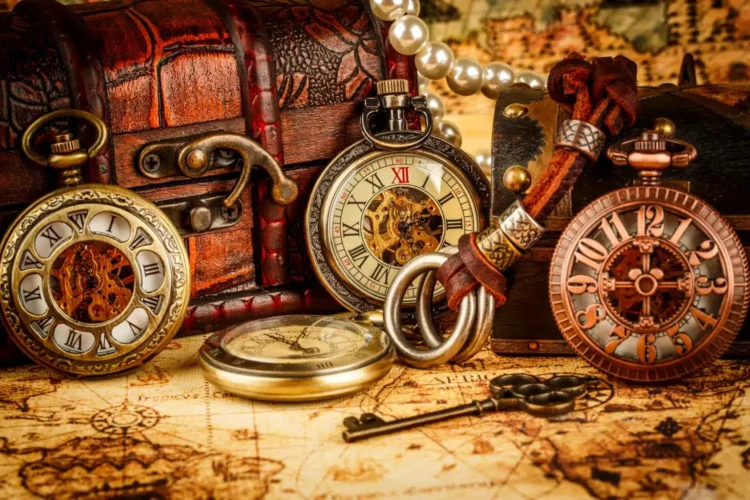 Imagem mostra relógios antigos de bolso sobre um mapa, com uma chave e dois pequenos baús ao lado, representando os tempos em que esses objetos eram comuns.